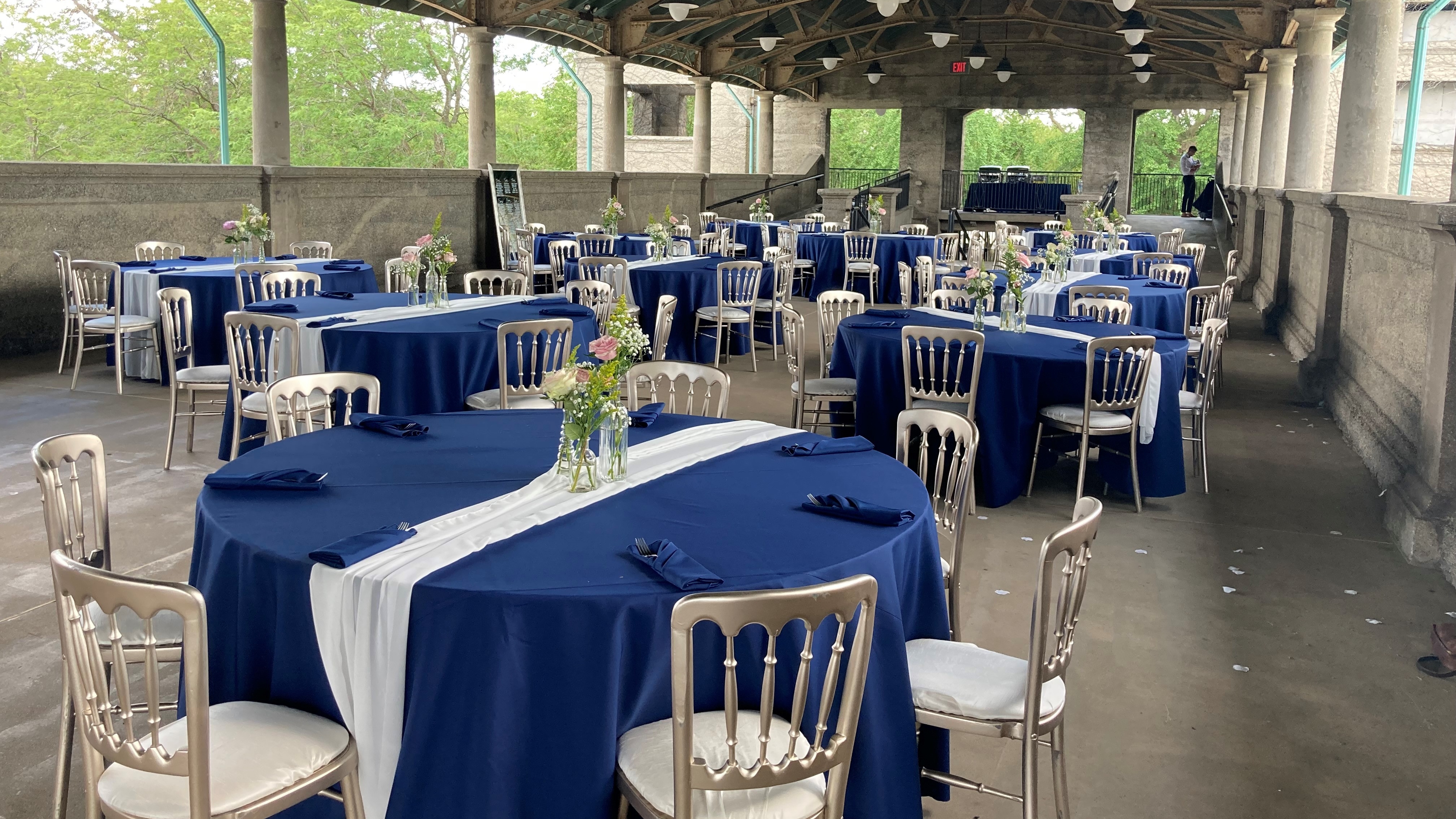 Outdoor wedding reception venue with round tables, navy blue tablecloths, and gold chairs.